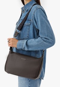 Borsa a tracolla in pelle marrone a graniglia con una texture liscia, dotata di una tracolla nera con dettagli del logo e una forma rettangolare elegante.
