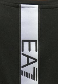 Must kangas, millel on vertikaalselt riide õmbluse kõrval valge lint musta kirjaga "EA".