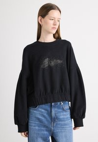 Felpa nera con orlo aderente, maniche oversized e design testuale decorato. Realizzata in tessuto morbido, presenta un classico collo a giro.