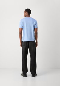 Light blue short-sleeve t-shirt, round neckline, paired with wide black pants. Fabric appears smooth, casual design.