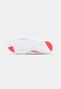 Valkoinen lenkkarin pohja punaisilla yksityiskohdilla, teksturoitu kumipinta pidon takaamiseksi, mukana Nike-logo ja ruutukaavio tractionia varten.