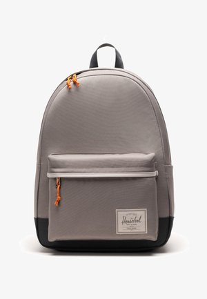 Gray fabric backpack with rounded shape, front zip pocket, orange zipper pulls, and a black bottom panel. Features a logo label on front.