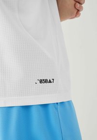 White mesh athletic shirt featuring a textured pattern and a black printed label with the text "030A7," paired with solid blue shorts.