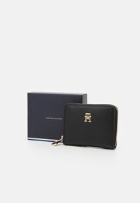 Schwarzes, mit Reißverschluss versehenes Geldbeutel aus Leder mit einem Logo in goldener Farbe auf der Vorderseite, inklusive passender navyfarbener Geschenkbox.