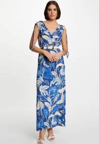 Robe maxi bleue avec un motif floral en blanc et bleu clair. Dotée d'un décolleté enveloppant, d'une taille ceinturée et de bretelles nouées aux épaules.