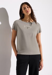 T-shirt gris à manches courtes avec le texte « FIND You », col rond, texture douce, associé à un pantalon noir texturé.