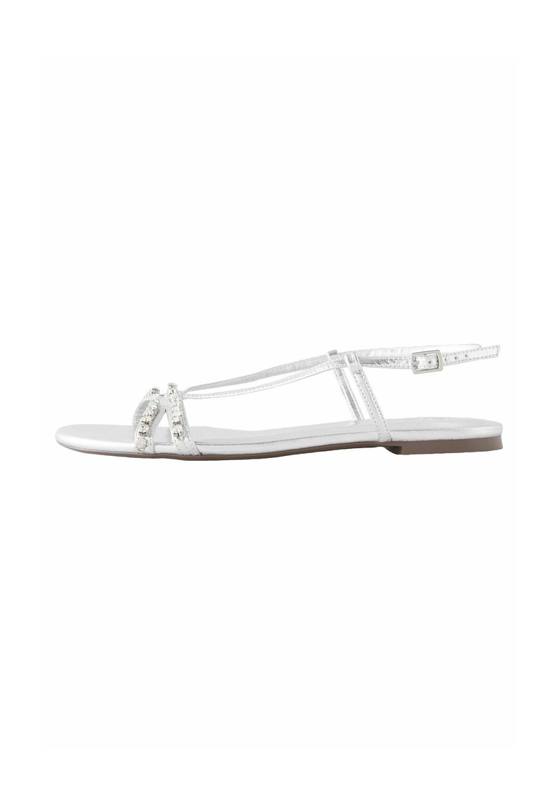 Weiße flache Sandalen mit metallischem Finish, ausgestattet mit zwei Riemen, die mit klaren Verzierungen geschmückt sind, und einem verstellbaren Knöchelriemen.