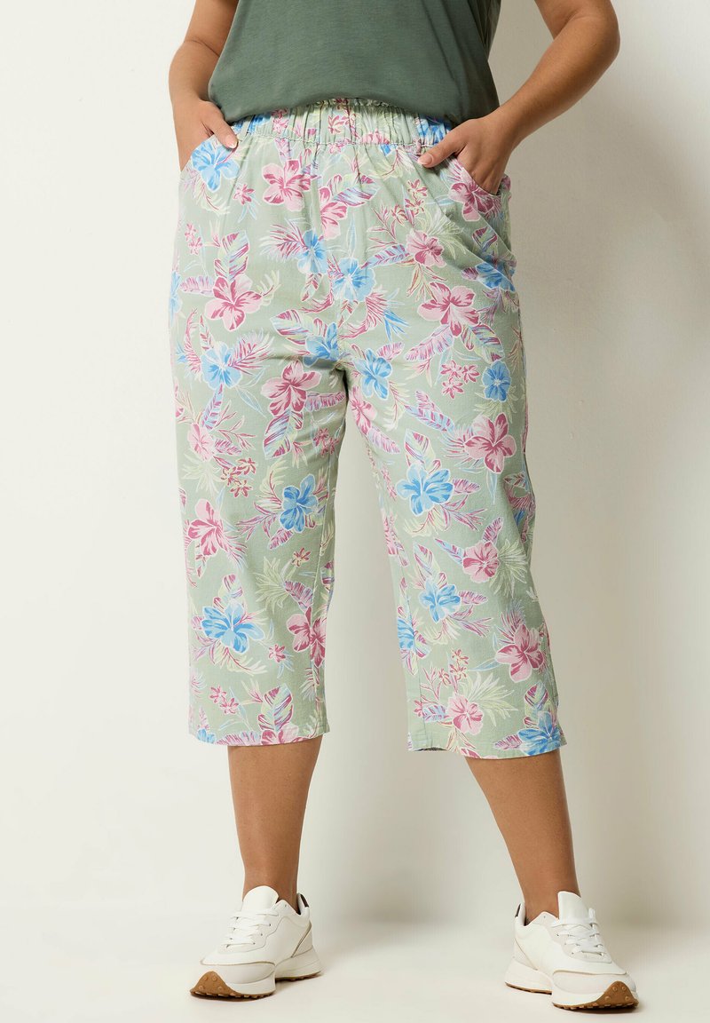 Onderlichaam met lichtgroene cropped broek met roze en blauwe bloemenprint, handen in zakken, gecombineerd met witte sneakers.