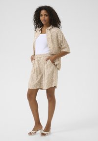 Beige vzorovaný set trička a šortek s uvolněným střihem, elastickým pasem, dvěma bočními kapsami a otevřenými sandály na podpatku s mašlí.