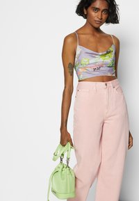 Um top cropped floral lavanda combinado com jeans de perna larga rosa claro. Segurando uma pequena mala verde com duas alças e fecho em cordão.