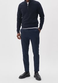 Granatowy sweter z zamkiem błyskawicznym, wykonany z miękkiego materiału, zestawiony z granatowymi spodniami typu slim-fit. Dodatki to czarne buty wsuwane. Prosty, nowoczesny design.