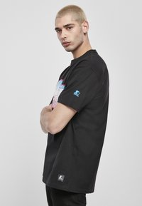 Fekete pamut póló rövid ujjakkal, elöl színes grafikával és bal ujján logós részlettel.