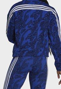 Chándal azul con un patrón y diseños abstractos en negro, con tres franjas blancas a lo largo de los hombros y los lados de las mallas.