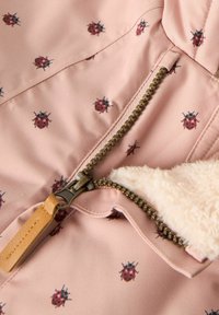 Roze stoffen jack met een herhalend lieveheersbeestje-patroon, een gouden rits met een leren trekhaak en een zachte, witte nepbontvoering.