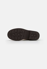 Semelle de chaussure en caoutchouc brun avec un motif de texture, présentant de profondes rainures et des accents triangulaires pour une meilleure adhérence et traction.