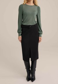 Grön stickad tröja med ribbade ärmar, parat med en svart blyertskjol med en framåt slits och bälte i midjan. Svarta knähöga stövlar.