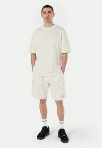 T-shirt de manga curta em bege claro e calções combinando, feitos de um tecido suave. Ténis pretos com detalhes brancos. Ajuste simples e descontraído.