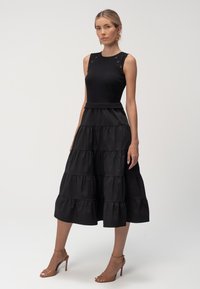 Czarna, warstwowa sukienka midi z prążkowanym tułowiem, okrągłym dekoltem i ozdobnymi guzikami. Gładki materiał z wyraźnie zarysowaną sylwetką i dołem.