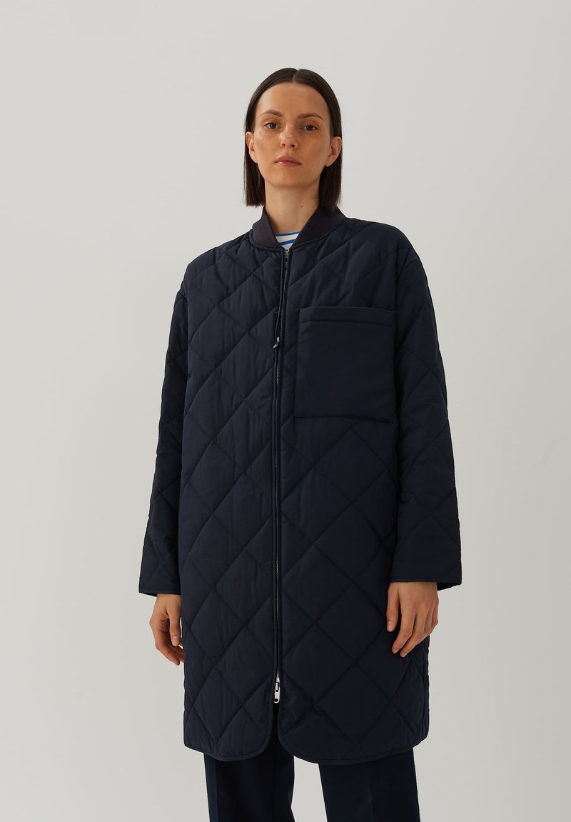 Gequilted marineblauwe jas met een hoge kraag, ritssluiting aan de voorkant en een borstzak. Heeft lange mouwen en een ontspannen pasvorm.