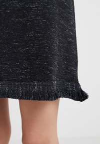 Falda de punto en azul oscuro con un acabado texturizado, que presenta un dobladillo con flecos. El material tiene un aspecto ligeramente moteado con acentos claros.