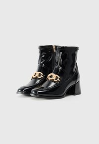 Sorte patentlær ankle boots med højglansfinish, medium høje blokhæle, og gylden kædeaccent hen over overdelen. Lynlåslukning bagpå.