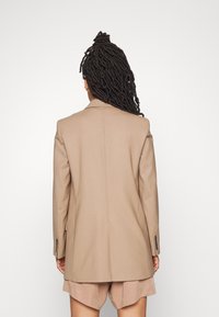 Blazer beige cintré avec un design structuré, revers crantés, fente unique au dos et poignets boutonnés, accompagné d'un short beige.