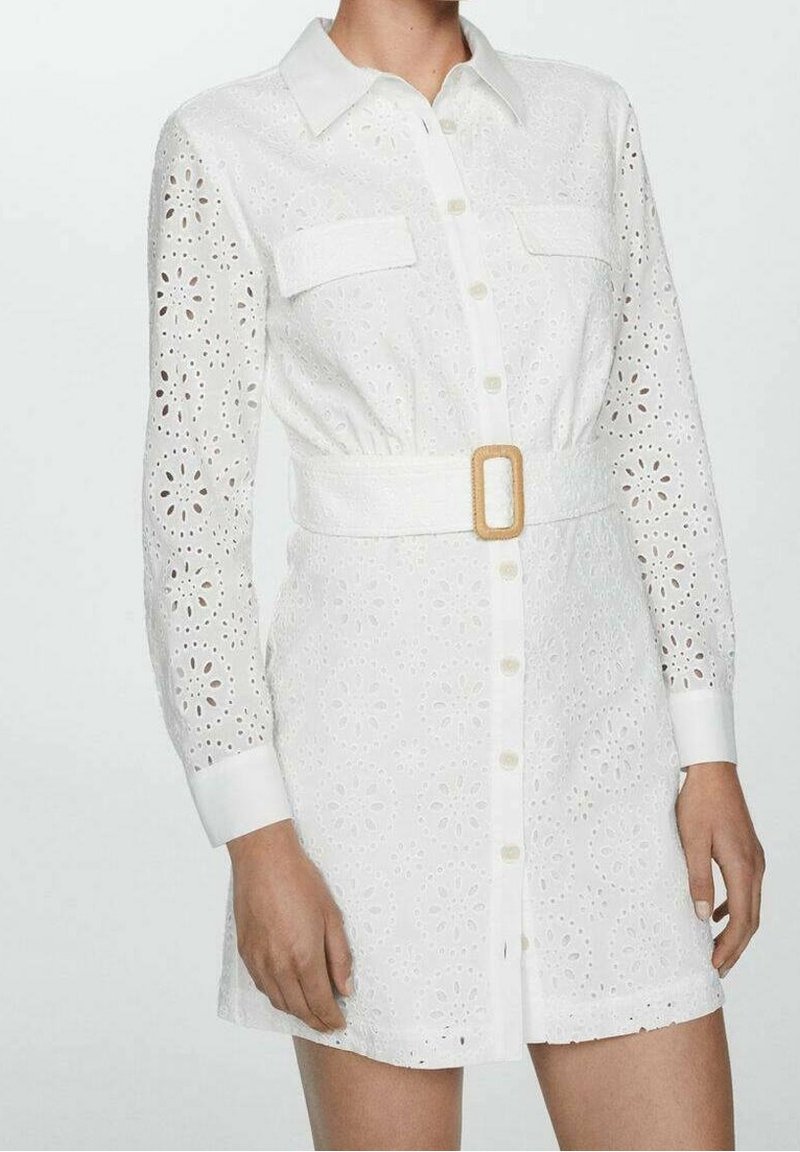 Abito camicia bianco con design a occhio di pernice, apertura con bottoni, due tasche sul petto, maniche lunghe e vita decorata da una cintura con fibbia rettangolare.