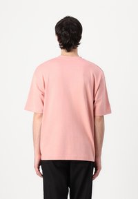 Ροζ ανοιχτό κοντομάνικο μπλουζάκι από μαλακό ύφασμα. Καθημερινή γραμμή, στρογγυλή λαιμόκοψη και απλή ραφή χωρίς ορατά λογότυπα ή σχέδια.