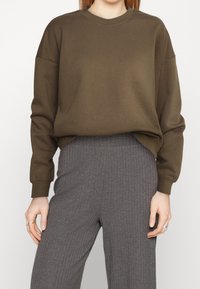 Felpa marrone con scollo a giro e spalle scese, realizzata in tessuto morbido. Abbinata a pantaloni grigi a coste, con vestibilità comoda.
