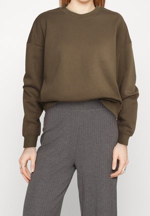 Sudadera marrón con cuello redondo y hombros caídos, hecha de una tela suave. Combinada con pantalones grises acanalados, que tienen un corte relajado.