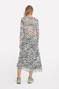 Langärmliges, transparentes Kleid mit schwarzen und braunen Zebra-Streifen; fließende Silhouette; kombiniert mit hellgrünen Turnschuhen.