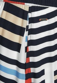 Raidallinen kangas, jossa on tummansinistä, valkoista, beigeä ja punaista väriä; sisältää pienen metallitaggin, jossa lukee "CECIL" sauman lähellä.