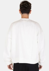 Felpa bianca oversize con spalle scese, polsini a costine e scollatura tondeggiante. Tessuto morbido con design minimalista, senza motivi visibili.