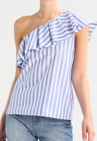 Top a righe blu e bianche con un design a spalla unica arricciato. Realizzato in tessuto leggero, presenta una vestibilità comoda e maniche corte.
