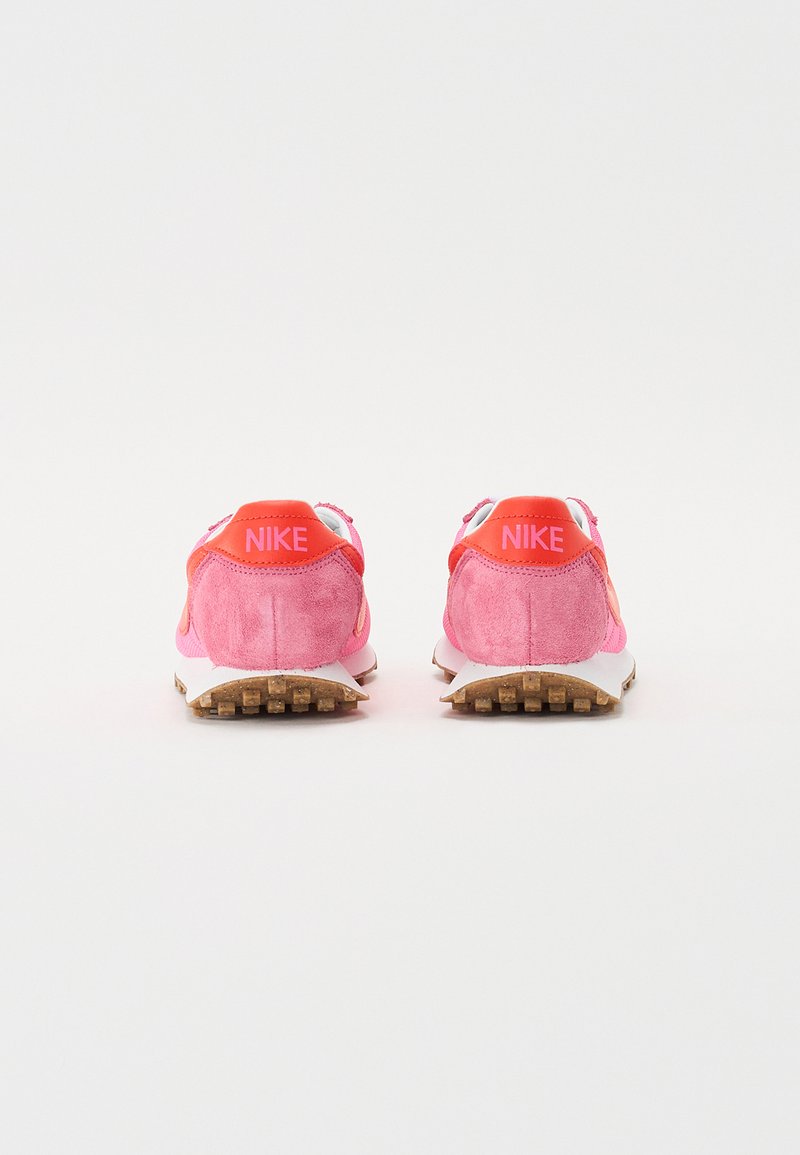 Zapatillas Nike rosas hechas de materiales de ante y malla, con una media suela blanca y una suela exterior de goma texturizada. Las etiquetas traseras muestran la marca "NIKE".