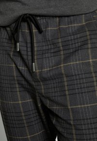 Czarno-szare spodnie w kratę wykonane z miękkiej tkaniny, z fakturowanym wykończeniem, elastycznym pasem i czarnym sznurkiem ze srebrnymi końcówkami.