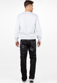 Felpa grigia a maniche lunghe abbinata a jeans neri in denim con dettagli di cucitura bianca e vari design di tasche, mostrata dal retro.