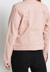 Rosa denimjacka med en kortad design, som har knapppdetaljer på ärmarna och fickorna, kombinerad med svarta jeans.