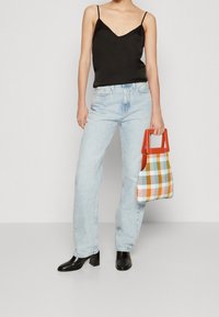 Camisola nera in satin, jeans a vita alta blu chiaro, e stivaletti neri con tacco. Porta una borsa a tracolla a scacchi multicolore con manici arancioni.