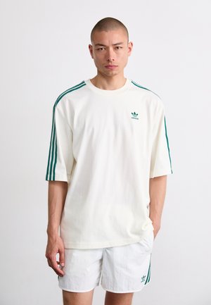 White cotton t-shirt with green three-stripe design on sleeves and small logo on the chest. Features a rounded neckline and relaxed fit.
