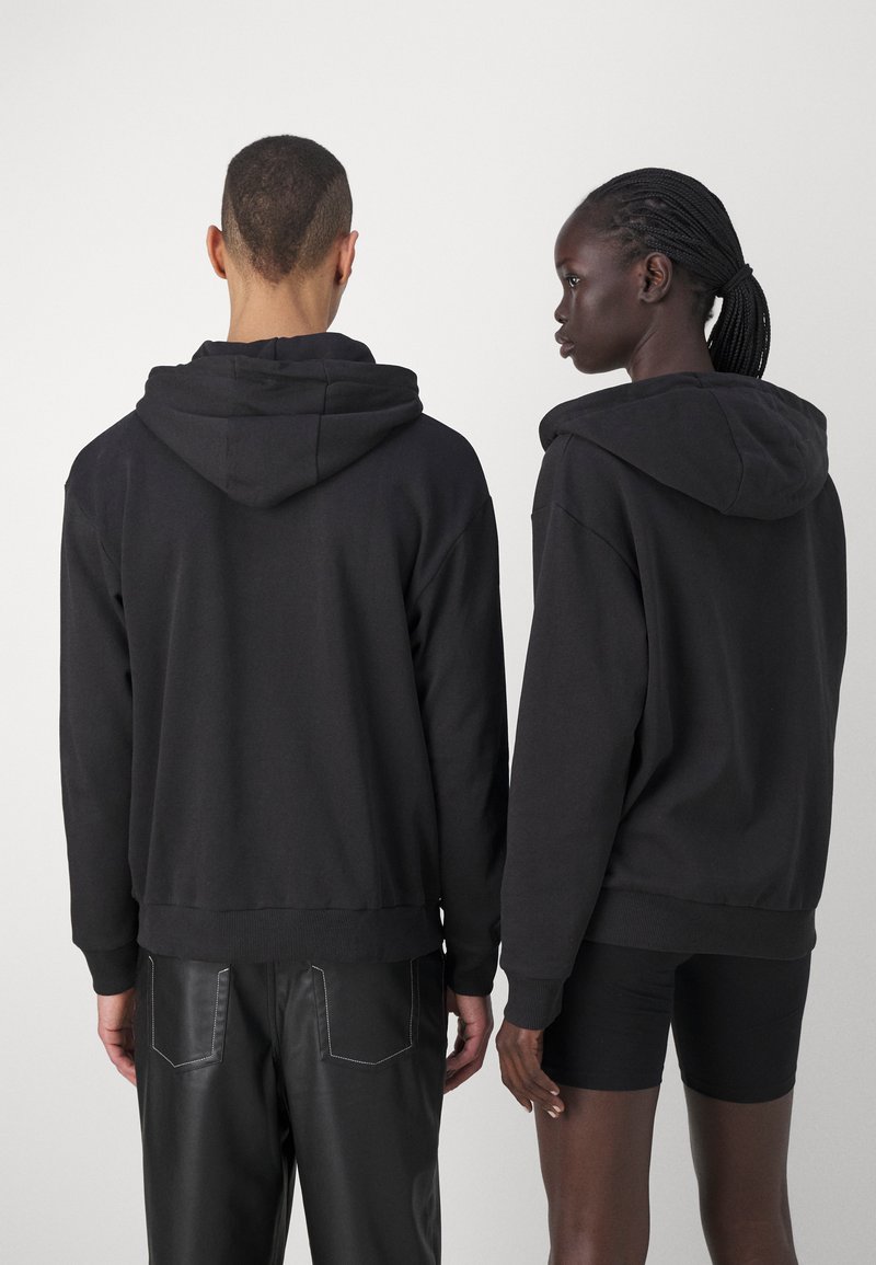 Felpe nere con cappuccio e vestibilità morbida, dotate di polsini e orlo a costine, cuciture visibili e una texture di tessuto morbido, fotografate da dietro.