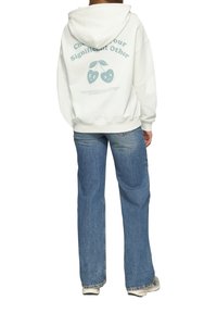 Witte hoodie met kersen graphic op de achterkant, relaxed fit, elastische manchetten, gecombineerd met lichtblauwe wijdlopende jeans.