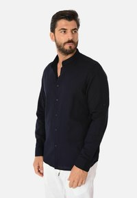 Camicia blu navy con colletto alla cinese, maniche lunghe e una texture liscia. Presenta dettagli con bottoni e una vestibilità su misura.
