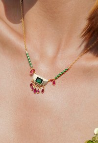 Collier en or avec une pierre rectangulaire verte, entourée de gemmes en forme de goutte rouge et d'accents rayés verts, suspendu à une chaîne délicate.