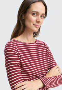 Rood en witte gestreepte longsleeve shirt met een bootnek en zachte stof, getoond met de armen over elkaar voor een lichte achtergrond.