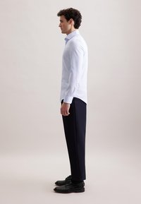 Lichtblauw gestreept shirt met lange mouwen en een moderne pasvorm, gecombineerd met een donkerblauwe broek en zwarte leren schoenen. Zijaanzicht.