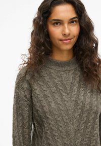 Pullover in maglia a treccia di colore verde oliva tenue, con colletto alto e motivi testurizzati, realizzato in un morbido misto lana.