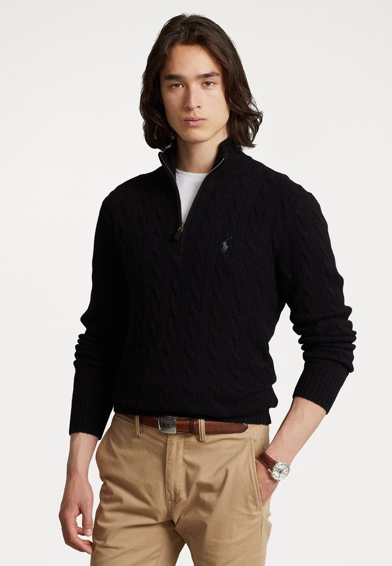 Black cable-knit sweater with a zip neck, featuring ribbed cuffs and hem; paired with light brown trousers and a silver watch.