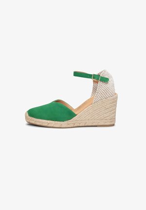 Sandalia de cuña tipo espadrille verde con puntera cerrada, tacón tejido beige y correa al tobillo con hebilla dorada sobre fondo blanco.