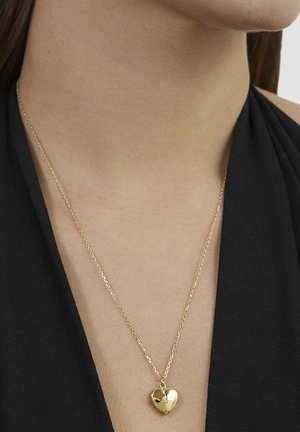 Goldenes Herzanhänger-Halskette an einer zarten Kette, mit polierter Oberfläche und dezentem Glanz, getragen vor einem dunklen Stoffhintergrund.